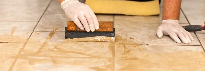 Person verfugt Fliesen mit Kelle.